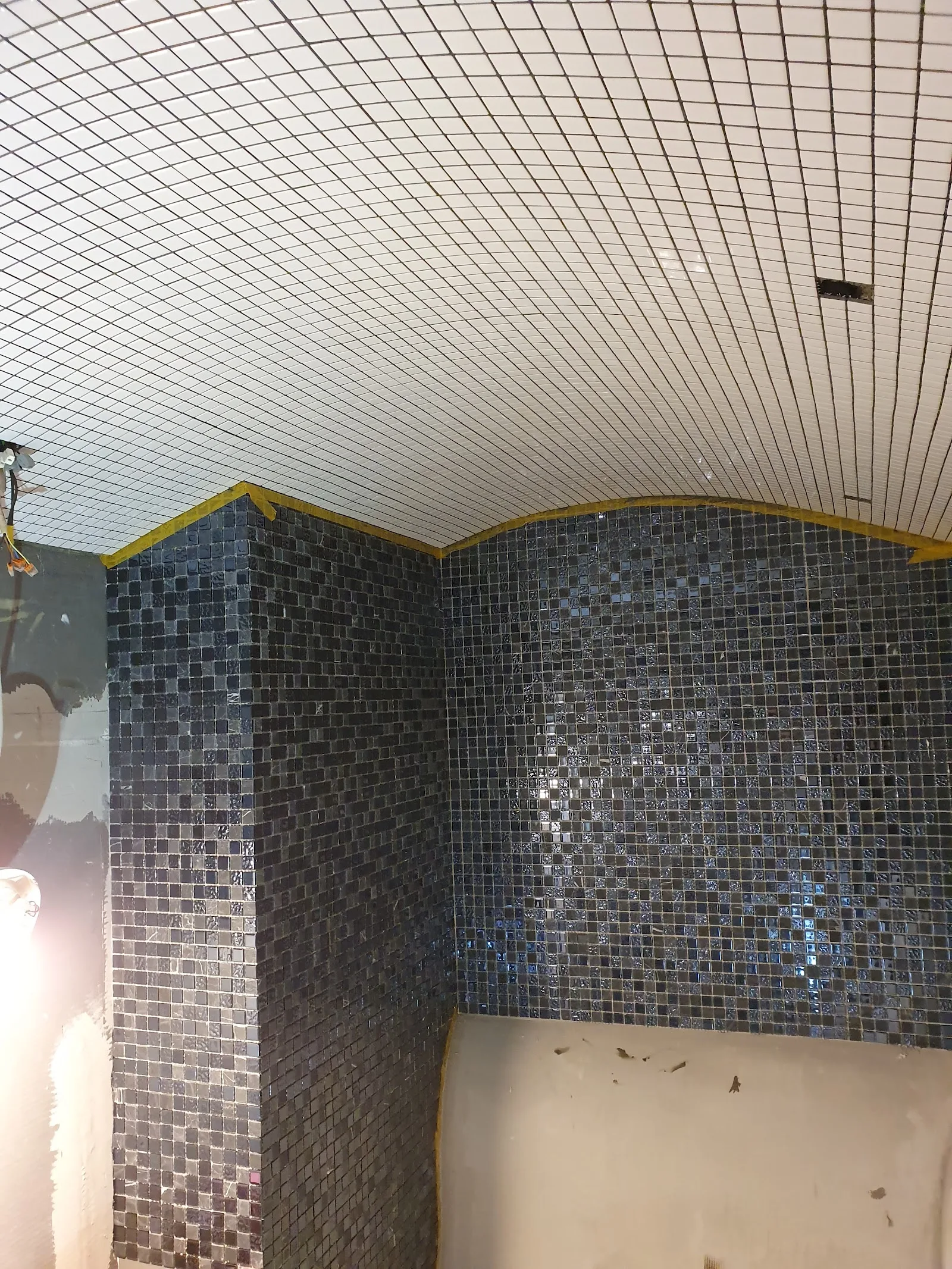 Bad im Bau mit weißer Mosaikdecke und dunkler Mosaikwand