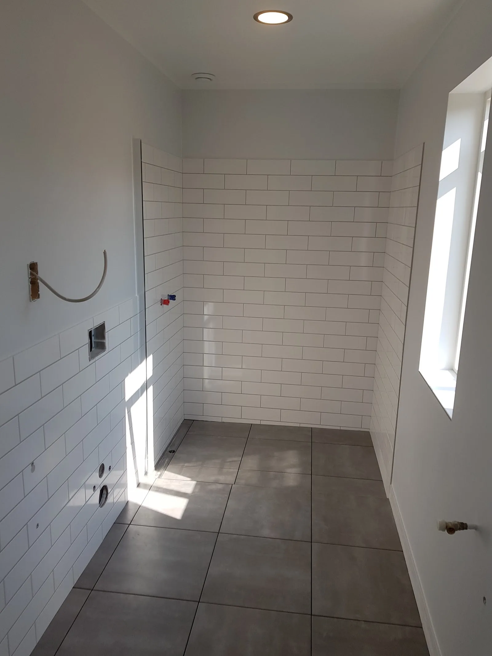 Fertige schmale Dusche mit weißen Fliesen und grauem Bodenbelag