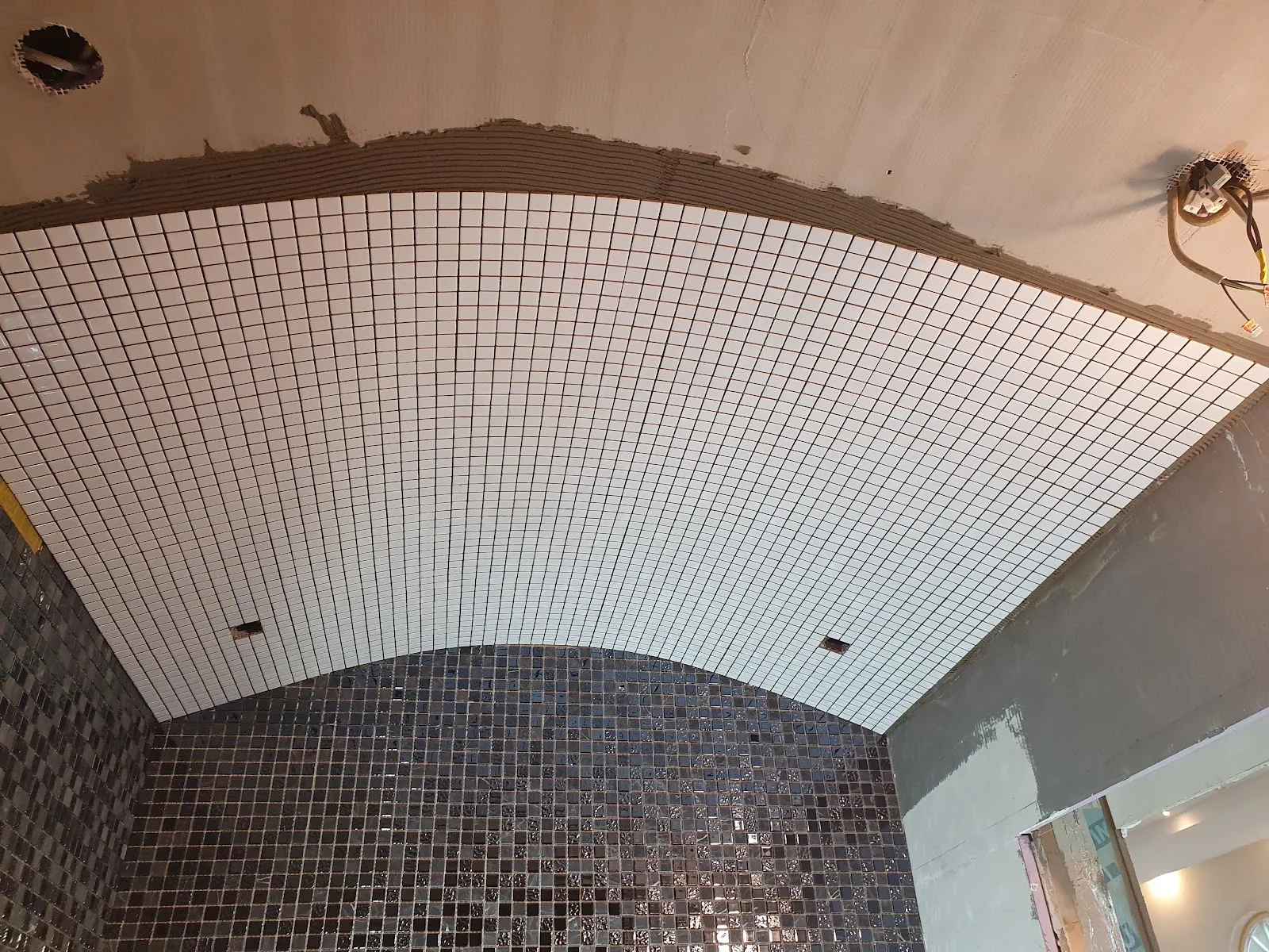Weißes Mosaik läuft in einer gewölbten Rundung an die Decke, im Verlegeprozess