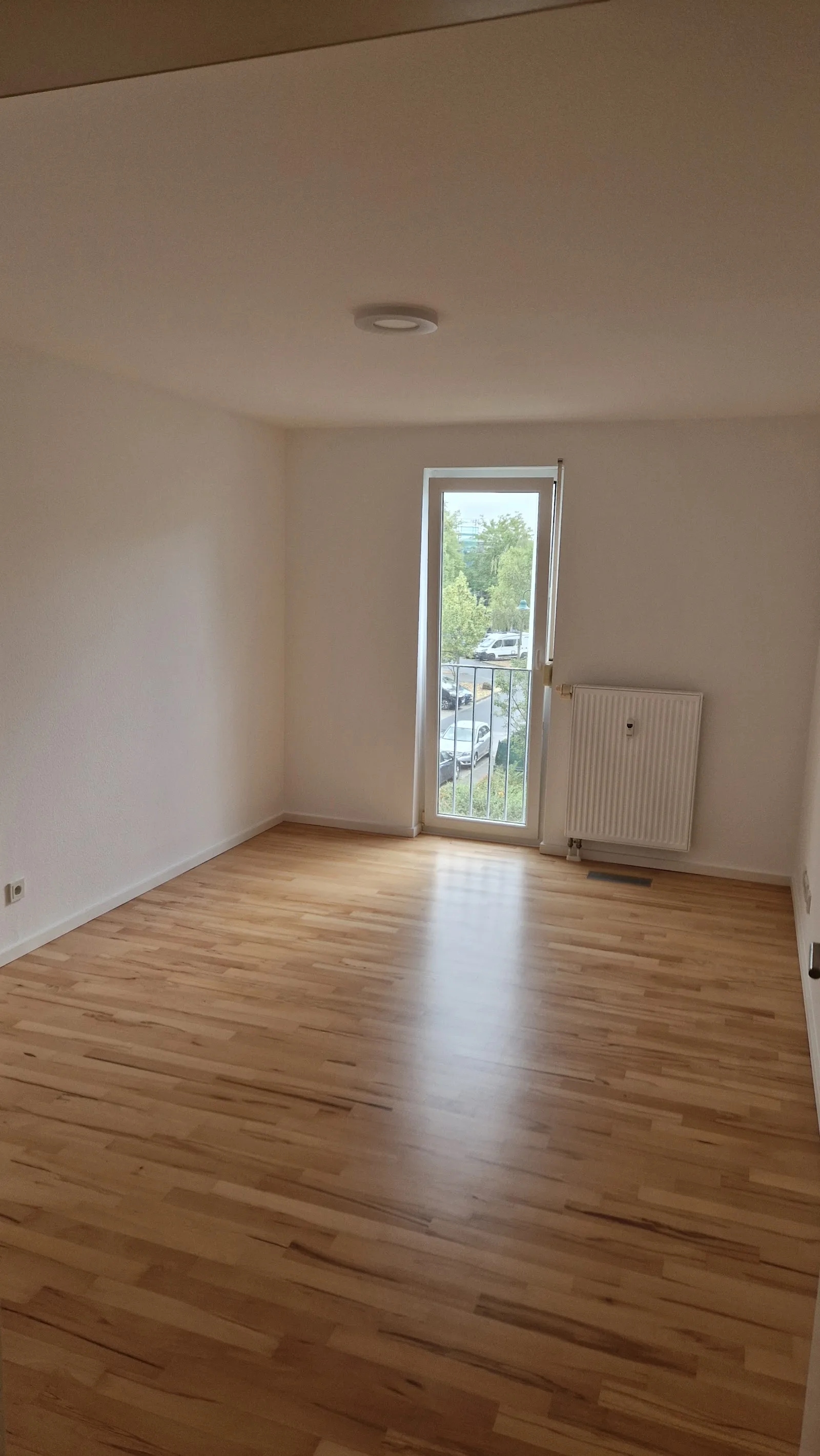 Leerer Wohnraum mit Balkontür und glänzendem Parkett