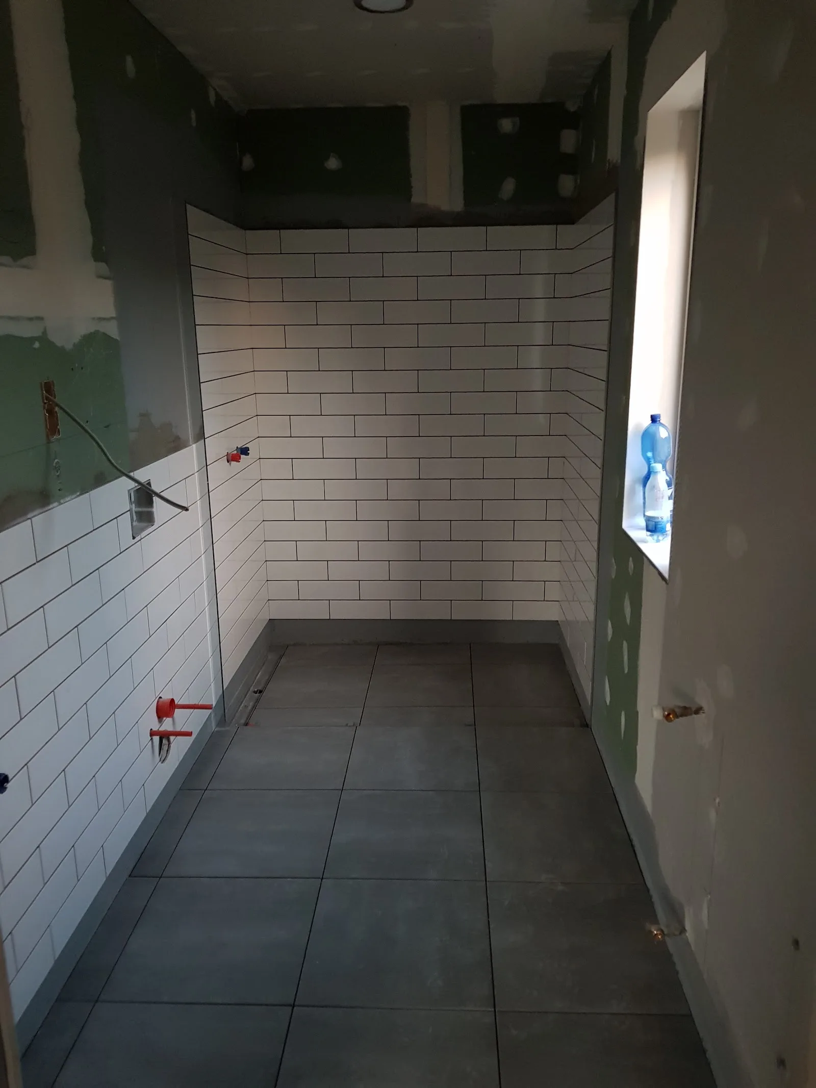 Fertige Dusche mit weißen Fliesen im Fischgrätmuster und dunklem Boden